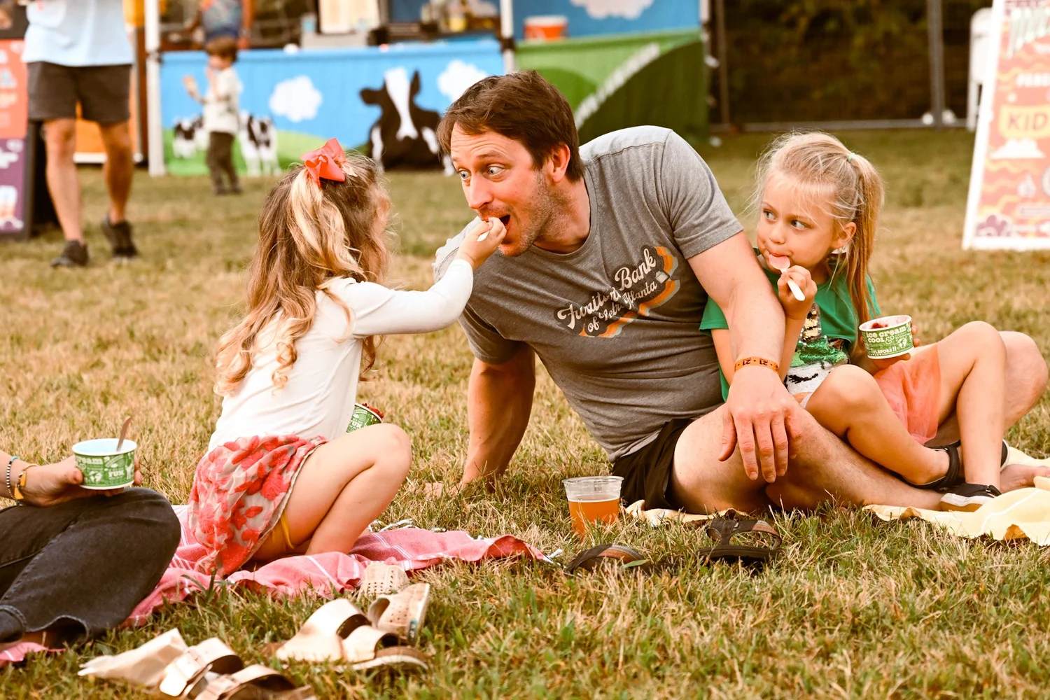 A dad getting fed ice cream by his daughters on the lawn at Touch of Brews 2023